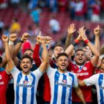 Um grupo de torcedores vestindo as cores do time Fluminense celebra um gol