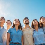 Grupo diversificado de pessoas sorrindo e olhando para cima ao ar livre em um dia ensolarado.