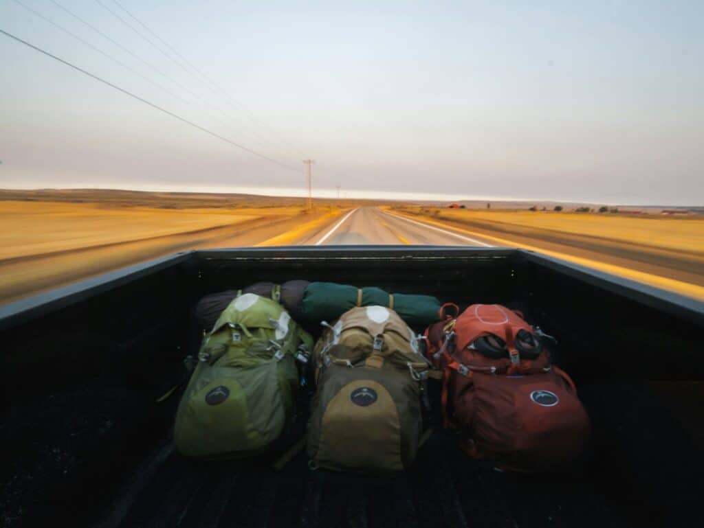 Mochilas de viagem na caçamba de uma caminhonete em movimento numa estrada deserta.
