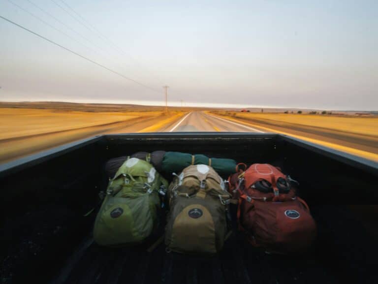 Mochilas de viagem na caçamba de uma caminhonete em movimento numa estrada deserta.