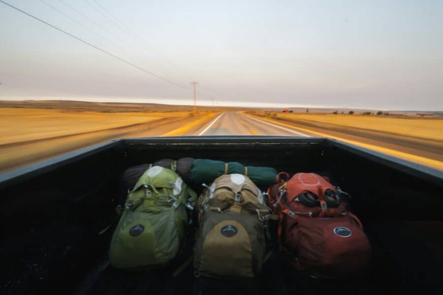 Mochilas de viagem na caçamba de uma caminhonete em movimento numa estrada deserta.