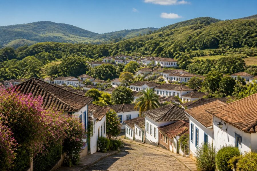 Vista panorâmica da cidade de Santana dos Montes cercada por colinas verdes, com casas coloniais de telhados vermelhos e vegetação ao redor.