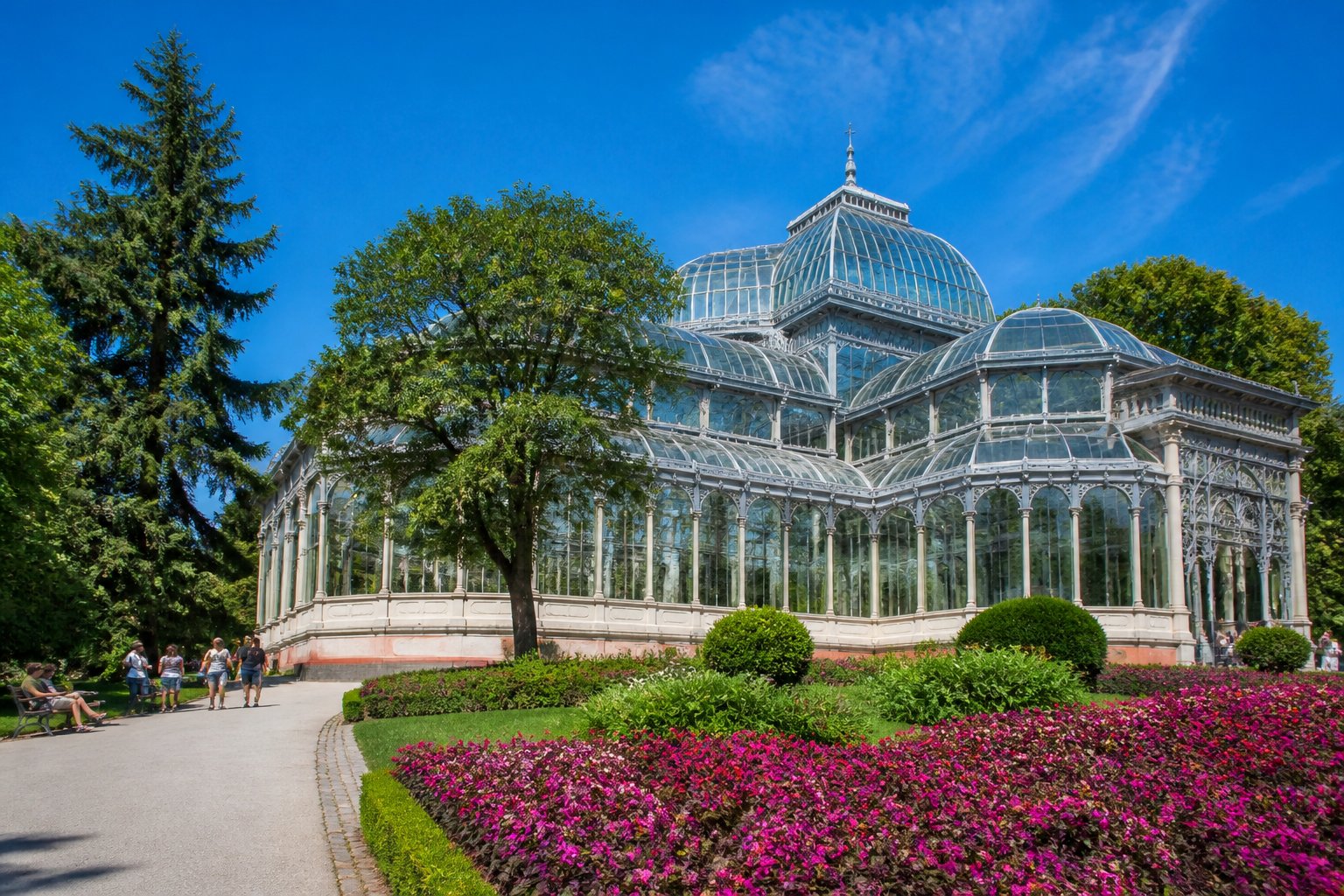 Vista do Palácio de Cristal em Porto cercado por jardins verdes e flores coloridas sob um céu azul claro.