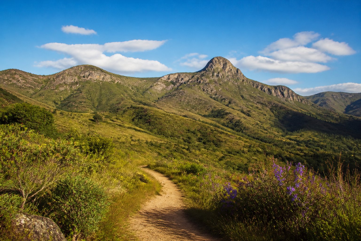 Paisagem natural das colinas verdes e montanhas de Serro, Minas Gerais, com céu azul e vegetação abundante.