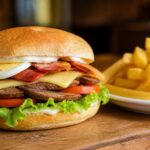 Sanduíche chivito com carne grelhada, queijo, bacon, alface, tomate, ovo e maionese, acompanhado de batatas fritas em um prato branco sobre uma mesa de madeira.