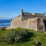 Forte Santa Teresa com suas paredes de pedra, grama verde ao redor e o oceano Atlântico ao fundo em um dia claro.