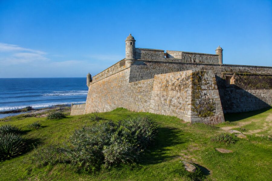 Forte Santa Teresa com suas paredes de pedra, grama verde ao redor e o oceano Atlântico ao fundo em um dia claro.